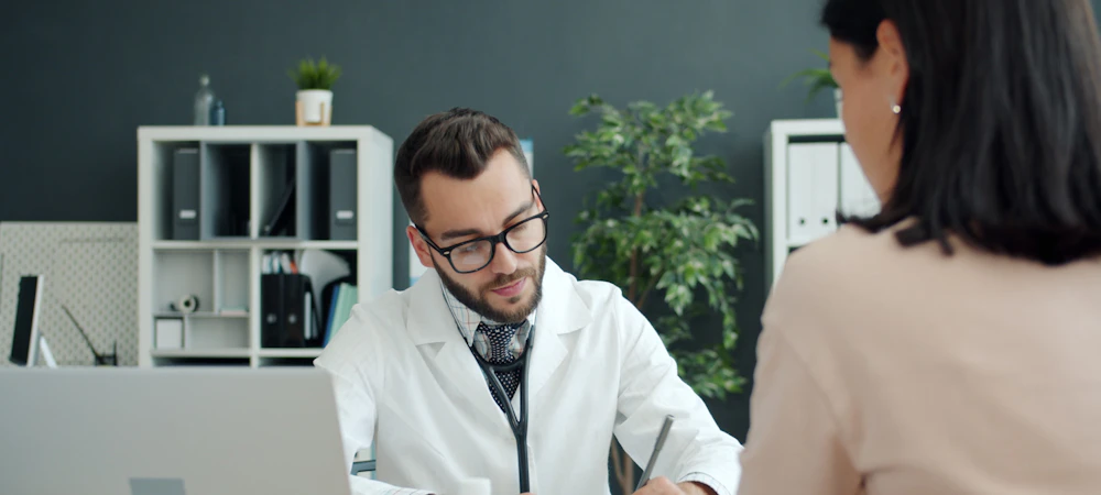 Médico tomando notas frente a una paciente en su consulta